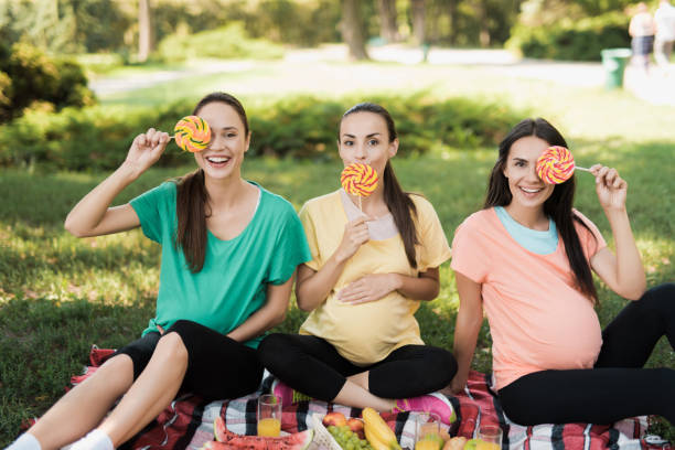 three pregnant women posing in a picnic park with large colored candies - human pregnancy outdoors women nature imagens e fotografias de stock