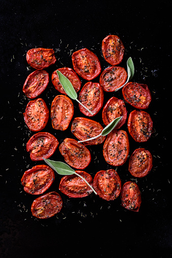 Oven roasted cherry tomatoes with garlic and herbs on a baking tray. Tomatoes confit appetizer. Top view.