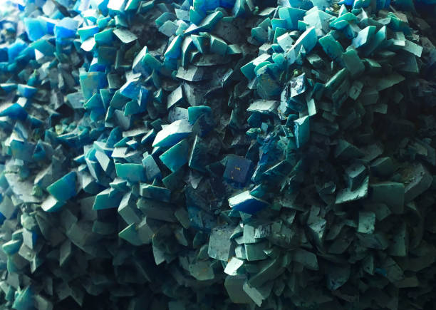 Macro shot of bright cyan-colored crystals contrasting with a dark rocky terrain.