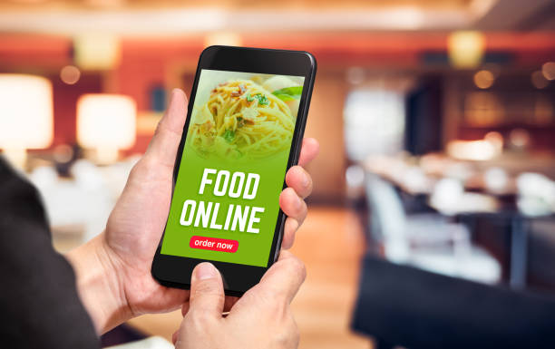 Close up hand holding mobile phone with order food online word on screen with blur restaurant bokeh light background,online food marketing concept. Close up hand holding mobile phone with order food online word on screen with blur restaurant bokeh light background,online food marketing concept ordering stock pictures, royalty-free photos & images
