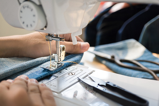 Closep up tailor process, women's hand working on sewing machine sew denim fabric