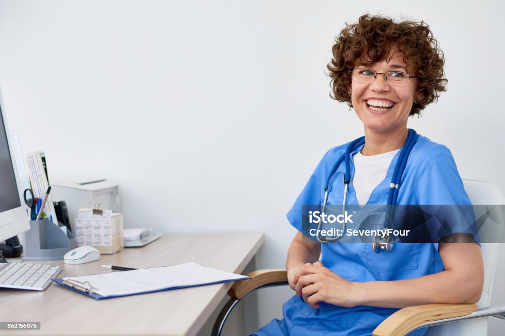 Laughing Female Doctor at Desk in Office Portrait of friendly female doctor sitting at desk in office  and laughing happily, copy space Doctor Stock Photo