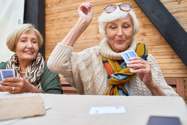 Happy Old Lady Winning Card Game Portrait of cheerful seniors playing card game at lunch table on outdoor terrace, focus on two old women winning game poker card game photos stock pictures, royalty-free photos & images