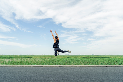 rear view of energetic man jumping against green field