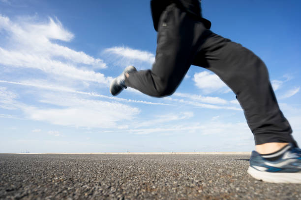 young male runner running on asphalt road against sky.