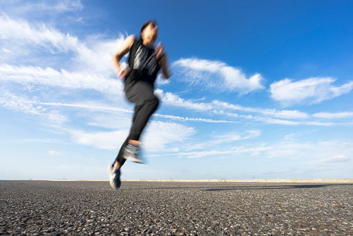 young male runner running on asphalt road against sky.