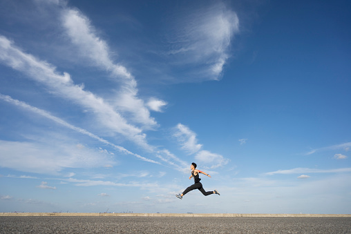 young male runner running on asphalt road against sky.