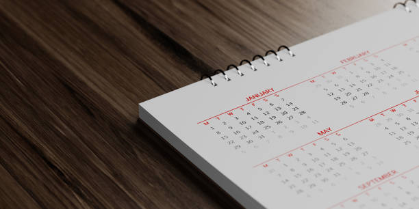 White Calendar On  Brown Wood Surface White calendar on brown reflective wood surface. January, May and February months are visible. Panoramic composition with copy space. Calendar and reminder concept with selective focus. annual event photos stock pictures, royalty-free photos & images