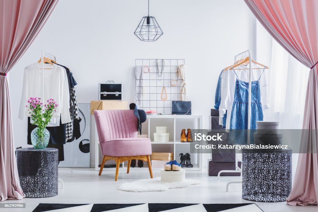 Pink chair in dressing room Pink chair in dressing room with flowers on designer table and clothes on hangers. Fashionable dressing room concept Closet Stock Photo