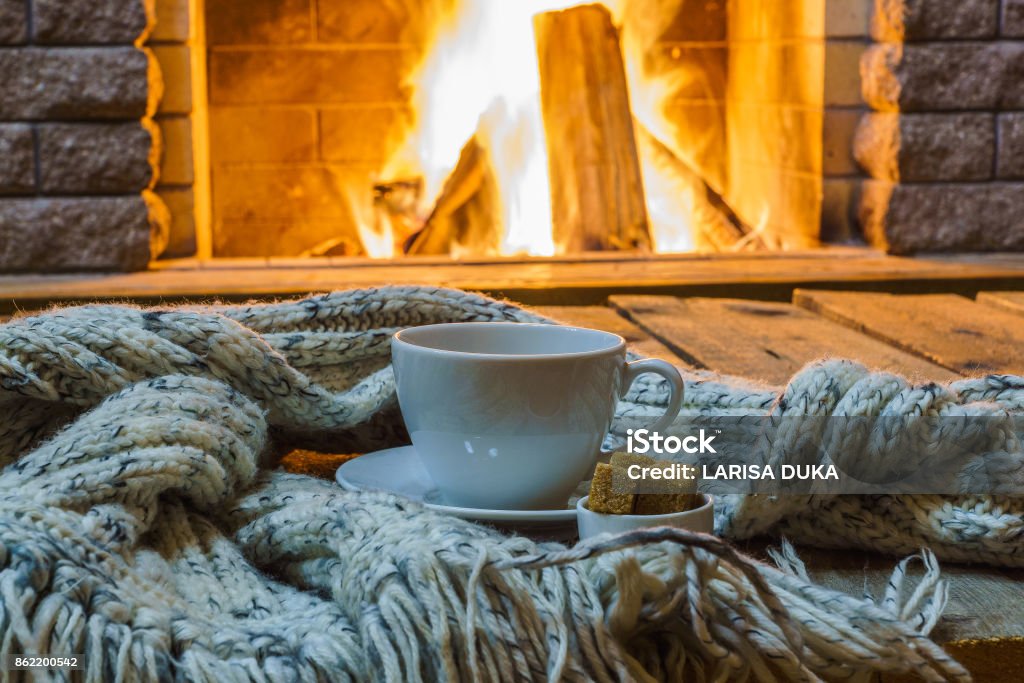 Cup of tea and sugar,  woolen things near  cozy fireplace. Cup of tea and sugar,  woolen things near  cozy fireplace, in country house, winter vacation, horizontal. Cozy Stock Photo