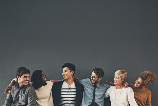 Studio shot of a diverse group of creative employees embracing each other against a grey background