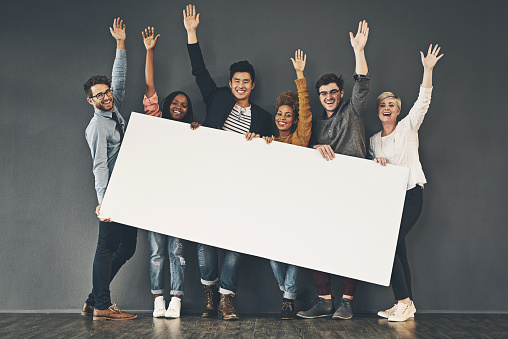 Studio shot of a diverse group of people holding up a placard against a grey background