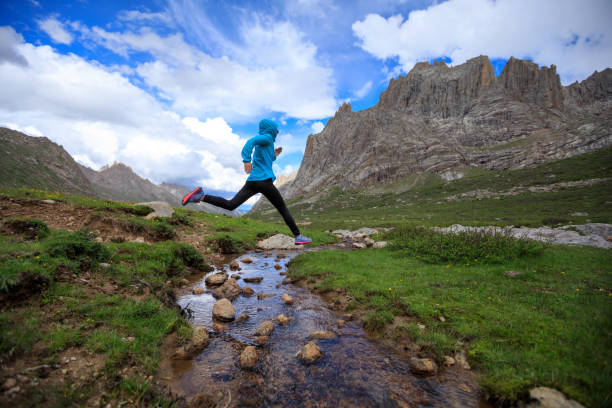 istock young woman trail runner jumping over stream water at mountain 862222126