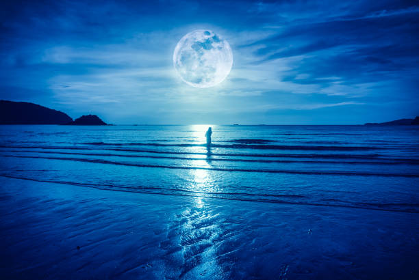 Super moon. Colorful blue sky with bright full moon over seascape and silhouette of woman standing in the sea . Serenity nature background, outdoor at gloaming. The moon taken with my own camera.