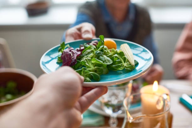 Close-up of family passing plate with fresh salad from leaves and vegetables