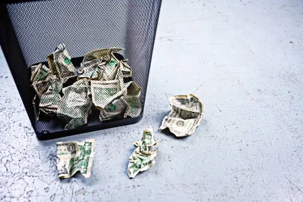 A trash can contains many American banknotes and more are abandoned alongside.