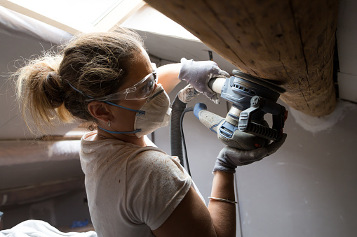 A woman sanding wooden beams in her attic