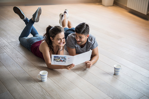 Happy couple reading catalogue while lying on the floor in their new apartment.