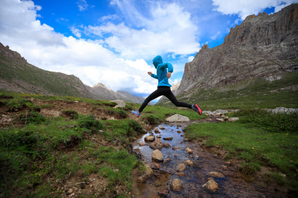 istock young woman trail runner jumping over stream water at mountain 862246274