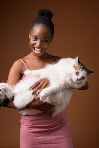 Studio shot of young beautiful African Zulu woman holding cute cat against colored background vertical shot