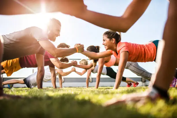 Low angle view of athletes cooperating while exercising on a sports training outdoors. Focus is happy couple.