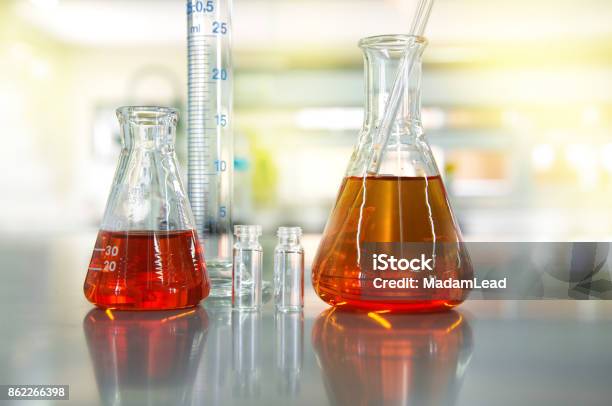 Orange Solution In Flask Cylinder Vial In Science Laboratory Background Stock Photo - Download Image Now