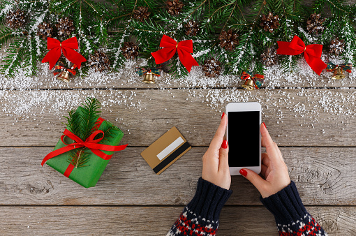 Christmas online shopping. Female buyer makes order at screen of smartphone with copy space. Woman buys presents for xmas eve. Winter holidays sales