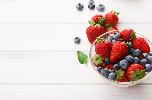 Assorted garden and wild berries. Mix of fresh organic strawberries, raspberries and blueberries in glass bowls on white wood with copy space