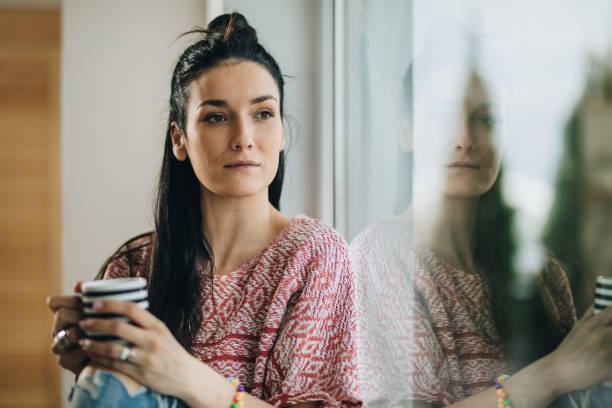 istock Beautiful pensive woman with coffee cup looking through the window. 862277106