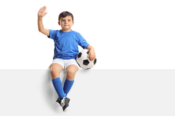istock Small boy with a football sitting on a panel and waving 862279516