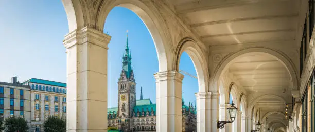 Arches above the restaurants and al fresco cafes of Alsterarkaden, overlooked by the iconic spire of the Rathaus in the heart of Hamburg, Germany’s vibrant second city.