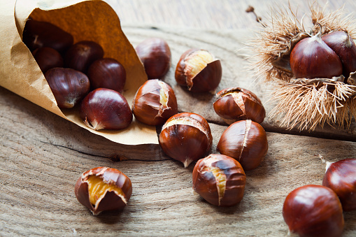 Traditional Christmas dish  - Ripe Sweet Roasted Chestnuts, cracked shells after put to the fire, natural paper and old wooden rustic background.