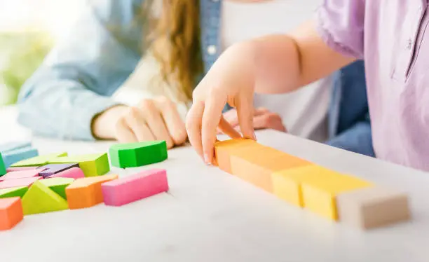 Girl playing with colorful toy wood blocks, her mother is helping her, education and fun concept