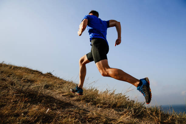 corsa dinamica in salita su sentiero atleta maschio runner vista laterale - running foto e immagini stock