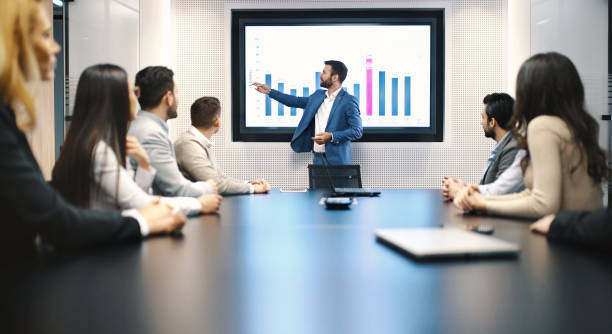 Board room meeting. Closeup of a board room meeting at a business company, usual scene at any modern company. There are six men and three women, one of the men is speaking in front of a large screen that's showing monthly revenue of their company. financial report photos stock pictures, royalty-free photos & images