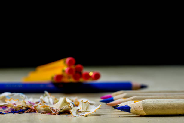 Top view of various wooden colored pencils arranged side by side on a semicircle shape beside a wooden sharpener on white background