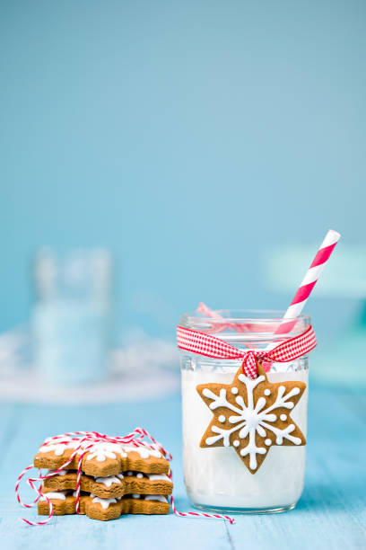 Cute gingerbread snowflake Christmas cookies with milk and straw over a blue background.