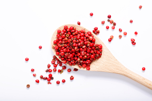 Organic Pink Peppercorn in wooden spoon on white background with copy space