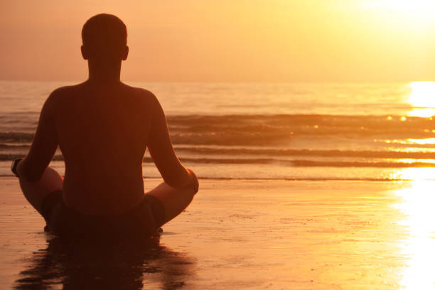istock Silhouette of young man meditating at sunset beach 862346374