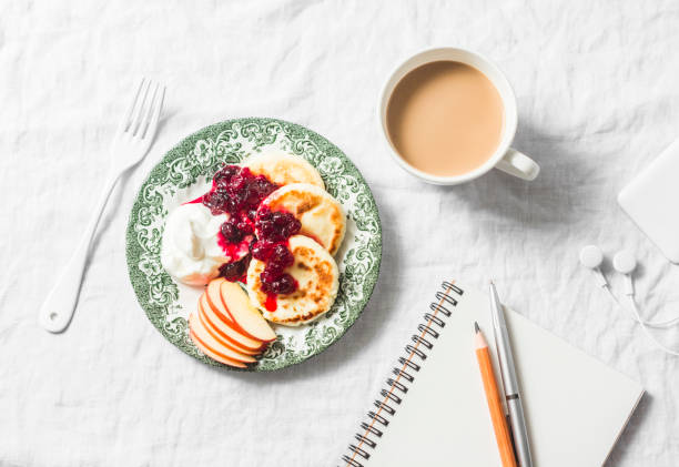 cottage cheese pancakes with greek yogurt and cranberry sauce, coffee with milk, notebook, phone with headphones on white table, top view. cozy morning breakfast - cranberry sauce audio imagens e fotografias de stock