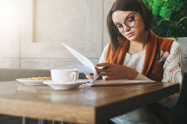 istock Front view.Young businesswoman is sitting in coffee shop at table,reading documents.Student is studying online 862354984