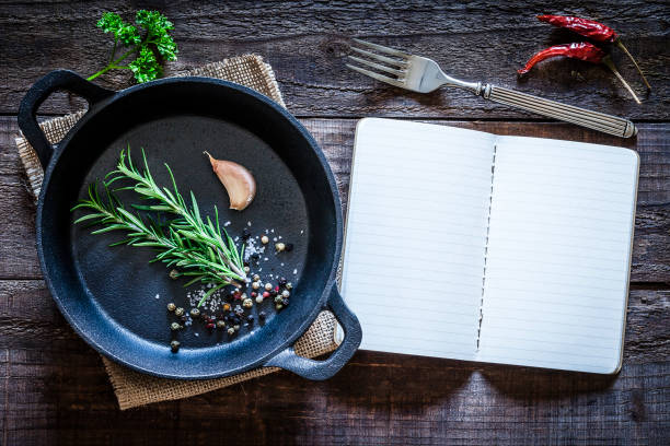 Cookbook and cast iron pan with some herbs on wooden table