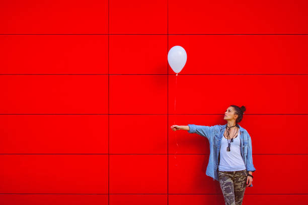 Young woman holding white balloon against the red wall stock photo