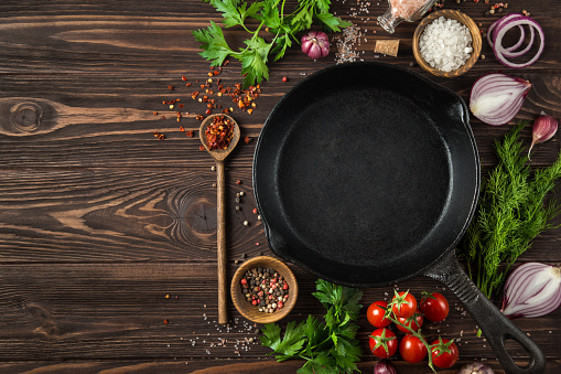 herbs and spices around cast iron skillet on wooden background.  Cooking concept. Top view. copy space