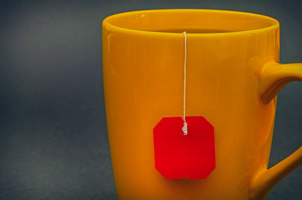 istock Yellow cup of tea with red teabag on gray background. 862377310