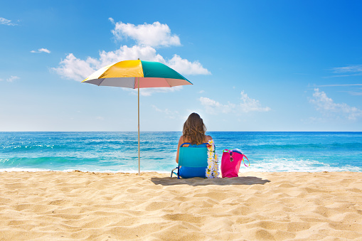 A woman in swimwear relaxing on the tropical beach. She is sitting on a beach chair sunbathing in Kauai, Hawaii