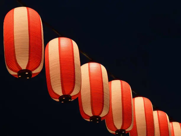 Paper red-white japanese lanterns Chochin hanging shines on dark nigrt sky background.