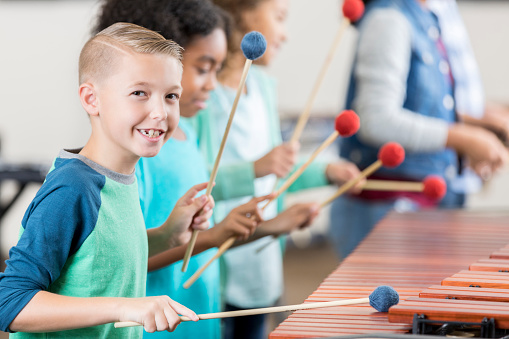 Cute Caucasian schoolboy smiles while playing marimba during orchestra class.