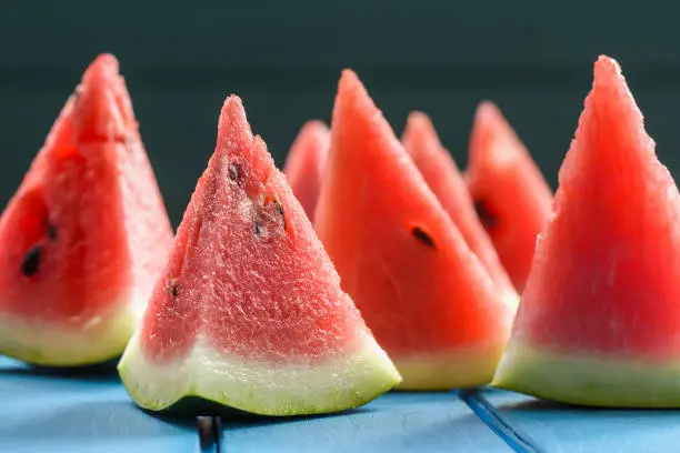 Vegan snack of fresh bright watermelon pulp cut into triangles on blue background closeup