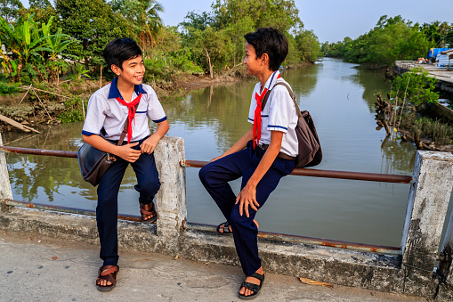 Two Vietnamese schoolboys sitting on a bridge, Mekong River Delta, Vietnam